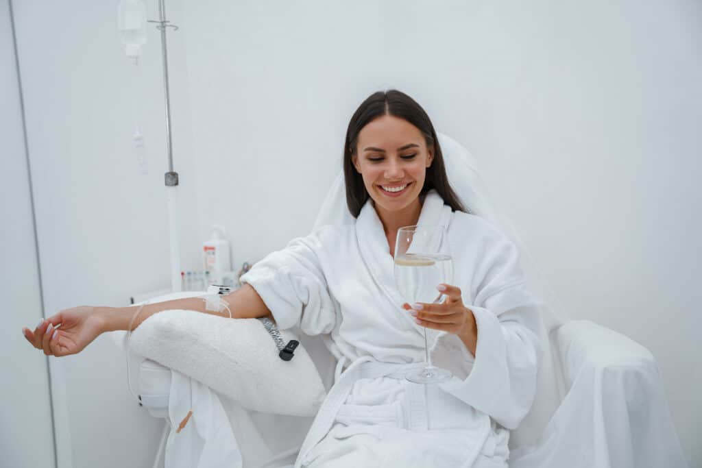 Beautiful woman in white bathrobe drink water during medical procedure in beauty clinic iStock 1421976368